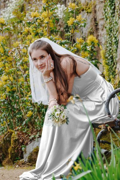 Im Licht der Blumen Braut in einem weißen Kleid mit Blumenstrauß, umgeben von gelben Blumen.