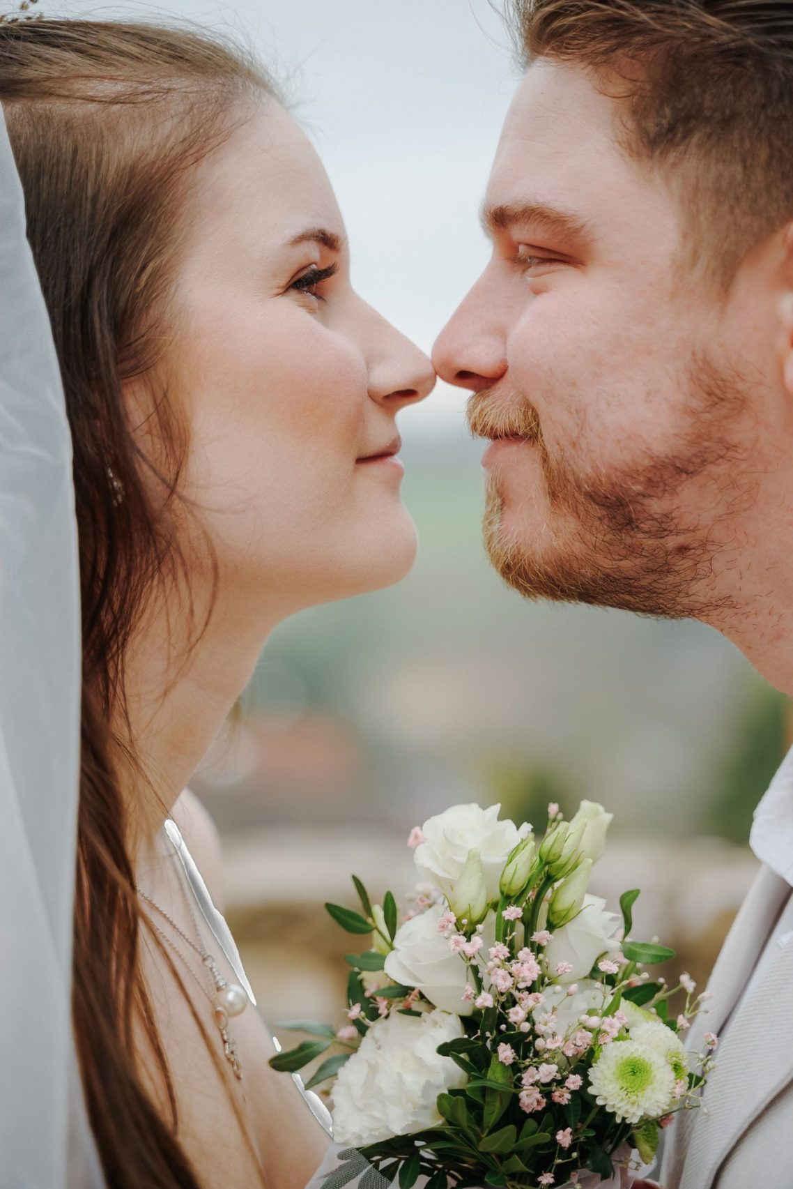 Brautpaar schaut sich liebevoll in die Augen, umgeben von Blumen und natürlicher Umgebung.