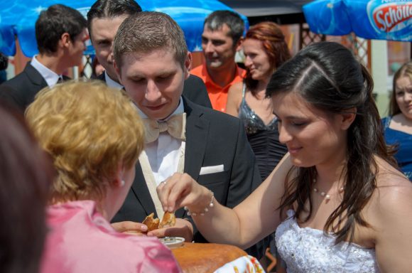 Ein russischer Hochzeitsmoment Brautpaar bei der Hochzeitsfeier vor einer Frau, die einen traditionellen Brotlaib mit Salz hält.