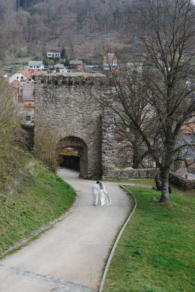 Ein neuer Weg beginnt Zwei Personen spazieren einen Weg zur alten Stadtmauer, umgeben von Bäumen.