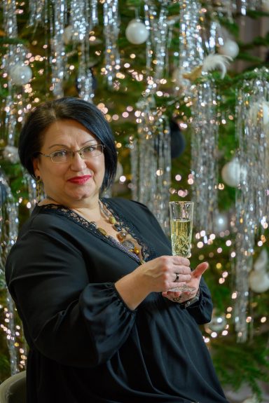 Frau mit Sektglas vor festlicher Dekoration und Lichtern.