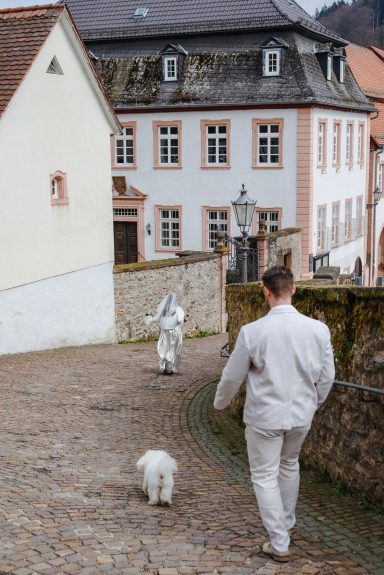 Der Moment der Flucht Mann in heller Kleidung geht mit Hund einen gepflasterten Weg, während die Braut sich von ihm entfernt und davonläuft.