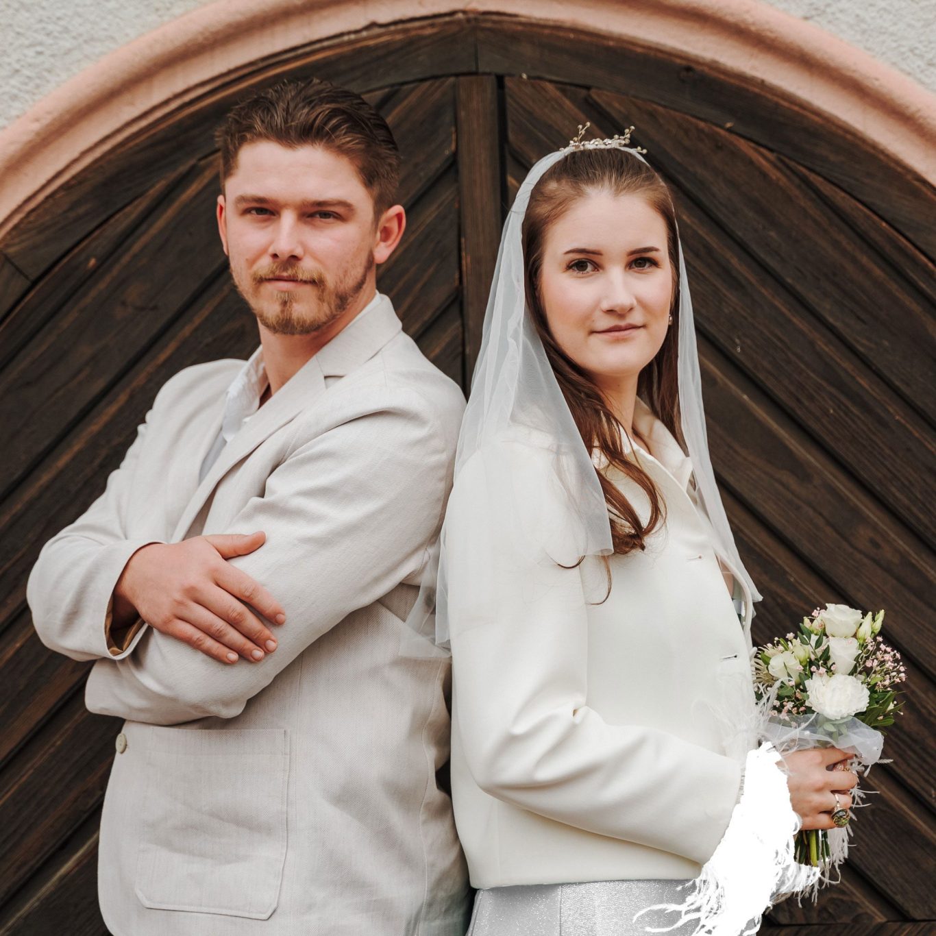 Getrennt und doch verbunden Brautpaar steht Rücken an Rücken vor einer Holz-Tür, Braut mit Blumenstrauß.